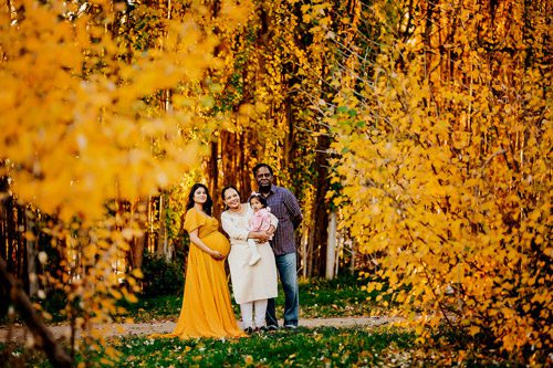 Canberra maternity photographer captures a serene portrait of a pregnant woman in a golden gown, surrounded by the warm hues of autumn foliage